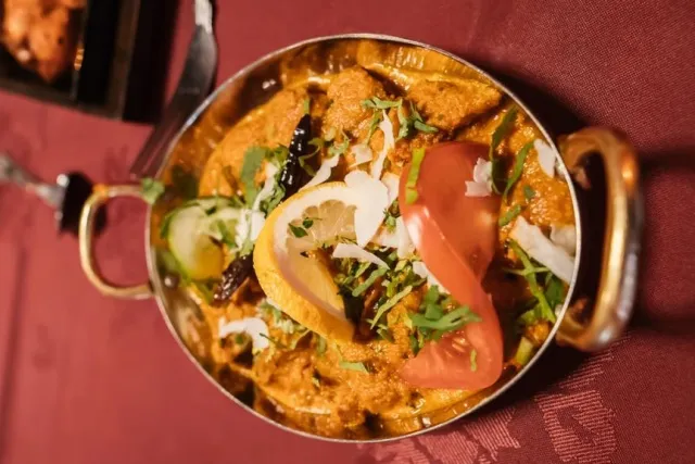 A brass kadai of curry, finished with coriander, lemon and tomato, on the restaurant's red cloth